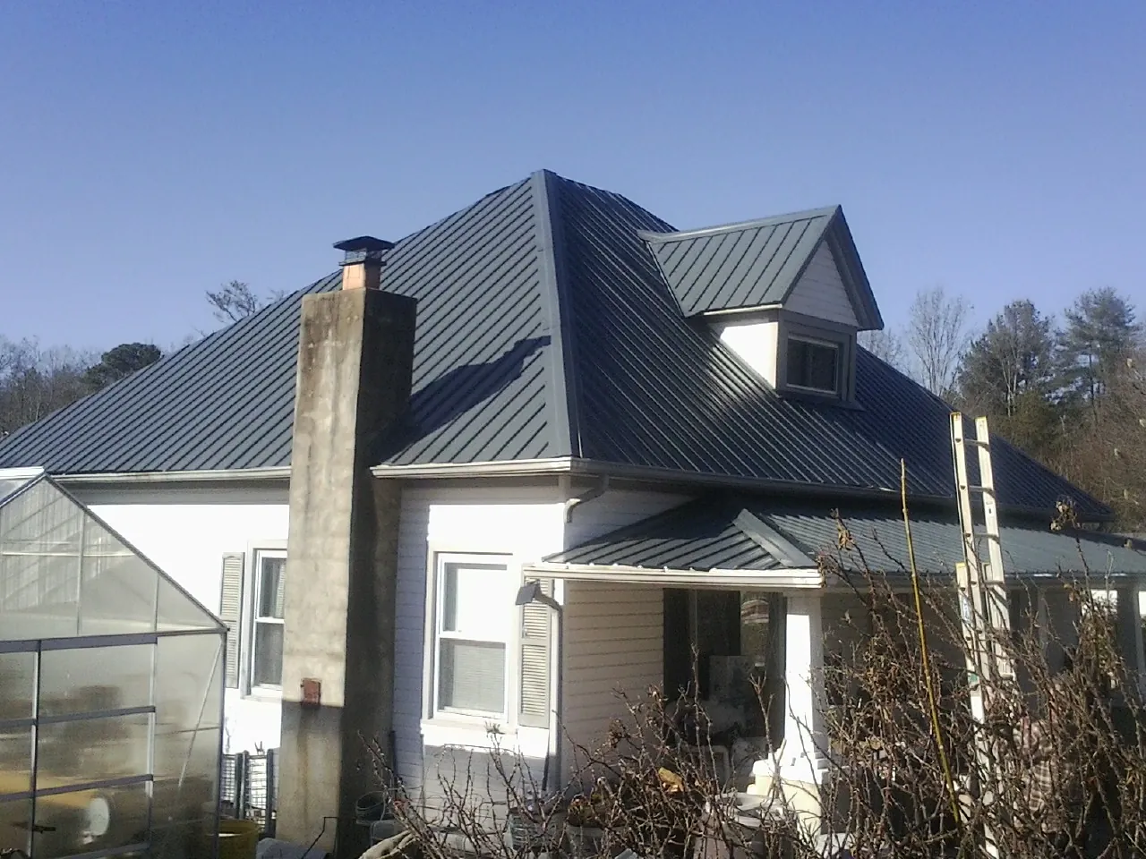 Dark blue standing seam metal roof on a white farmhouse with dormer — Slate & Tile Roof Repair by Roofing Brothers in Pattison