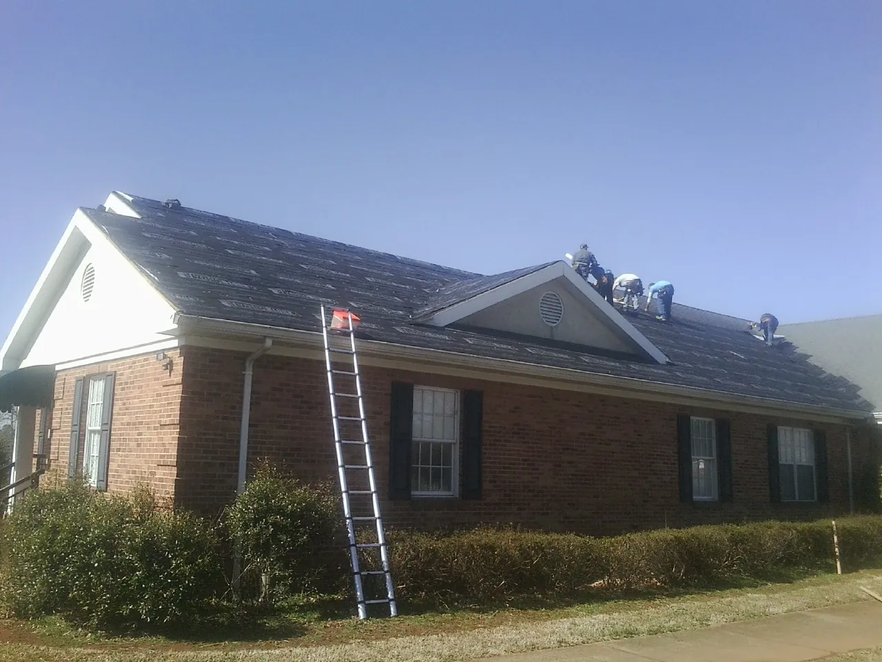 Crew tearing shingles off a brick ranch roof with a ladder set — Metal Roof Repair work by our crew in Pattison