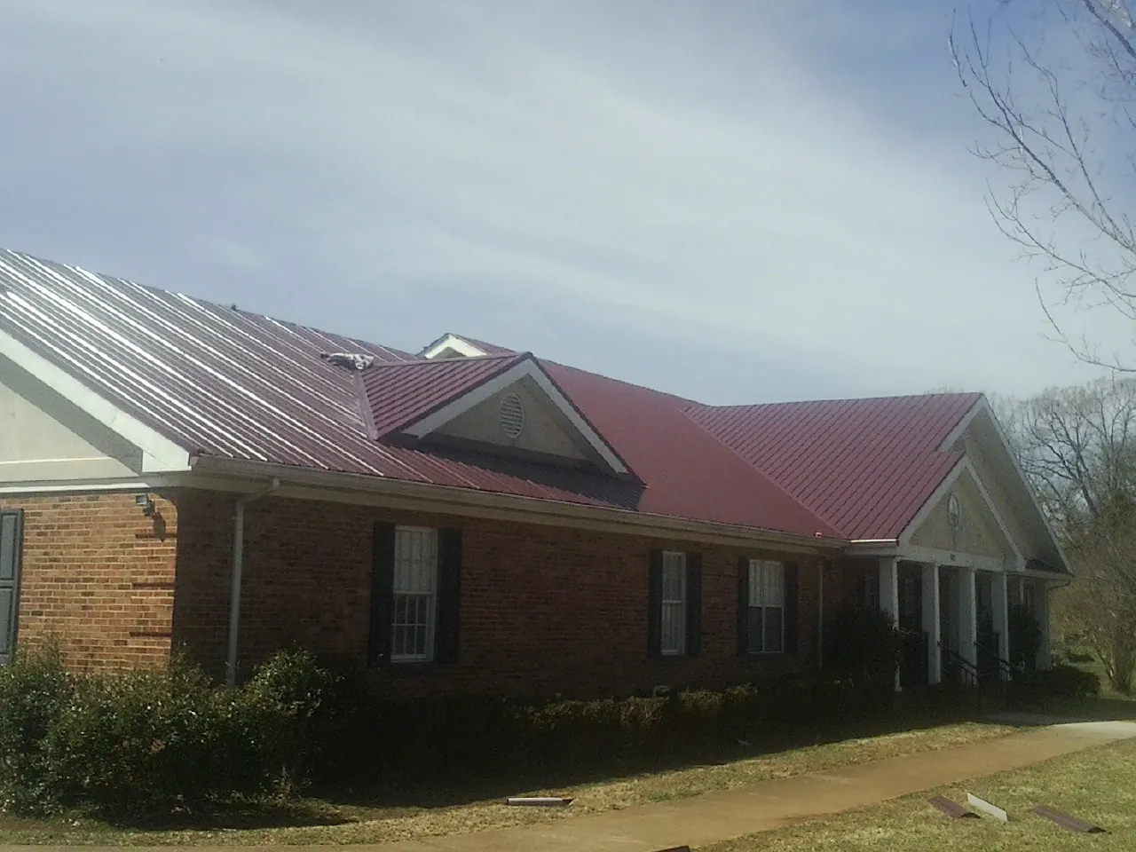 Red metal roof with gabled entries on a long brick building, from a Hail Damage Roof Repair job in Pattison