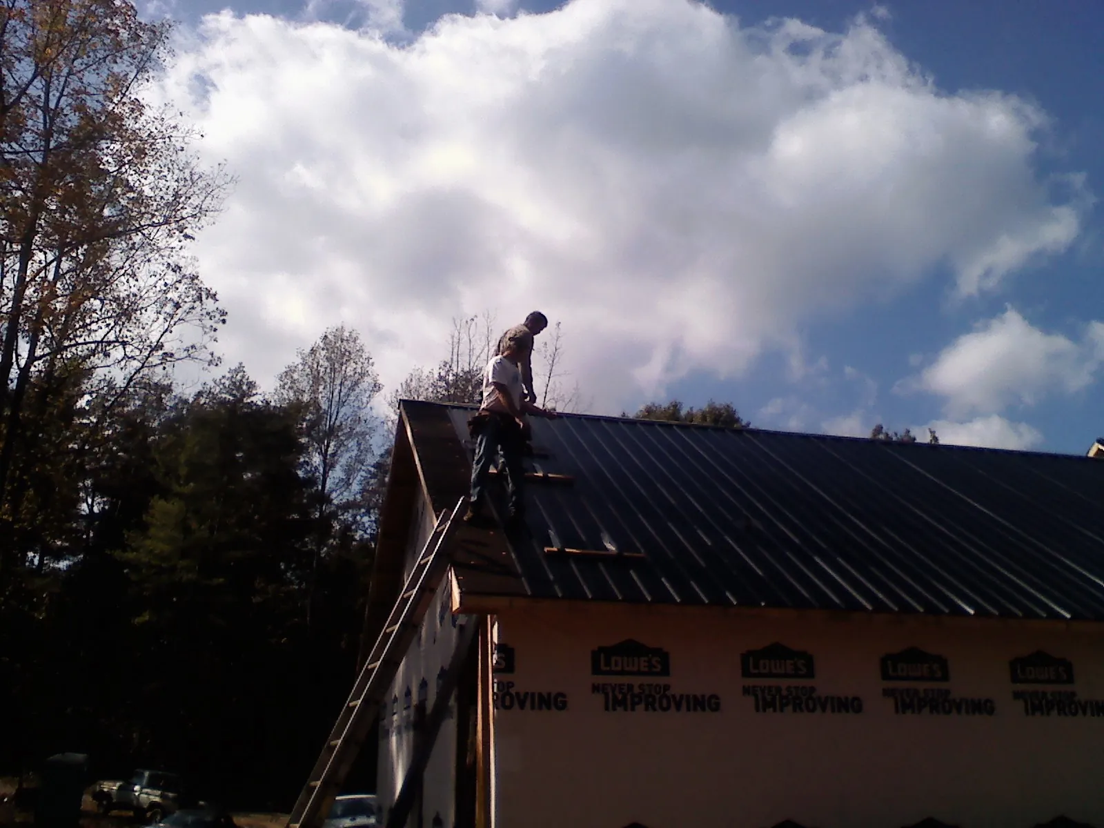Roofer fastening dark metal panels high against a cloudy sky, from a Roof Inspection job in Pattison